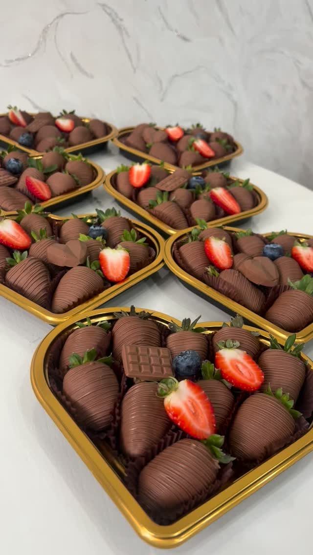 Chocolate-covered strawberries and blueberries arranged in heart-shaped gold trays on white surface.