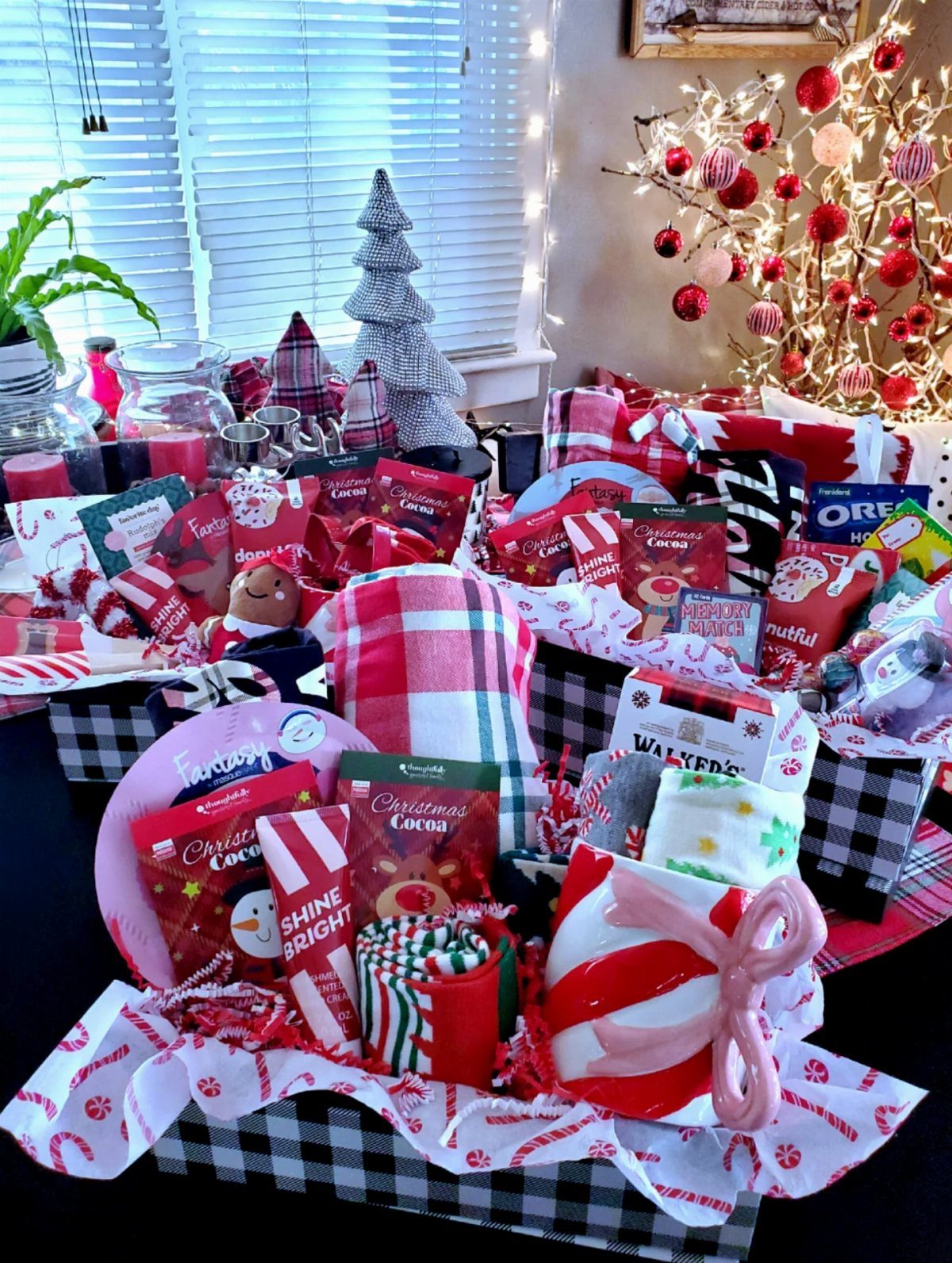 Christmas gift basket with cocoa, a striped mug, and red plaid blanket.