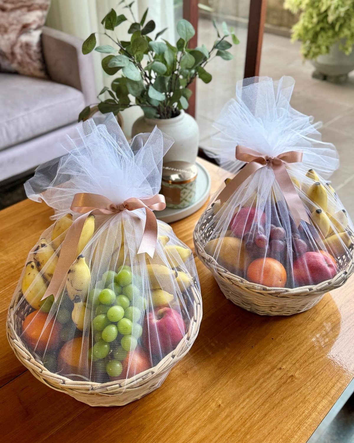 Two wicker fruit gift baskets wrapped in white tulle with peach ribbons.