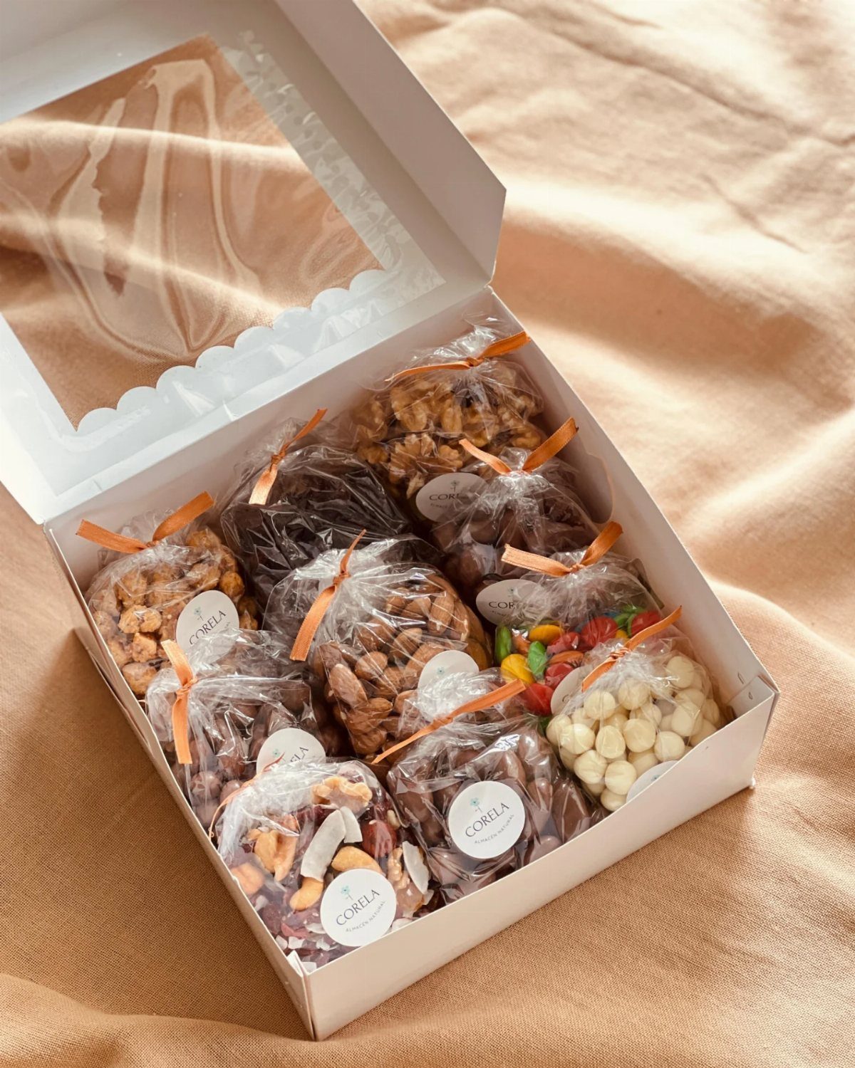 Assorted nuts and dried fruits in small bags inside a white gift box.