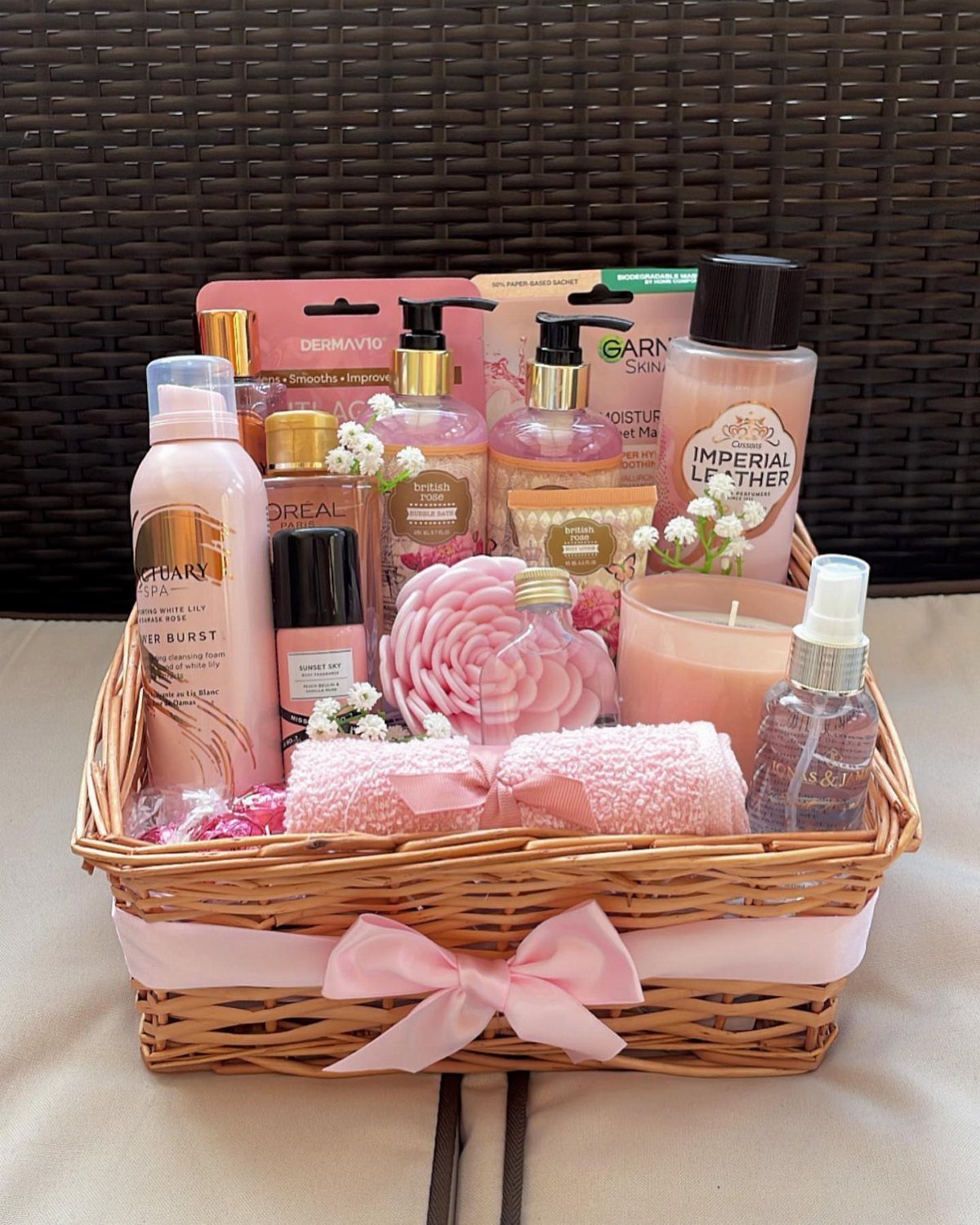 Wicker gift basket with pink ribbon containing beauty products, towels, and a candle.