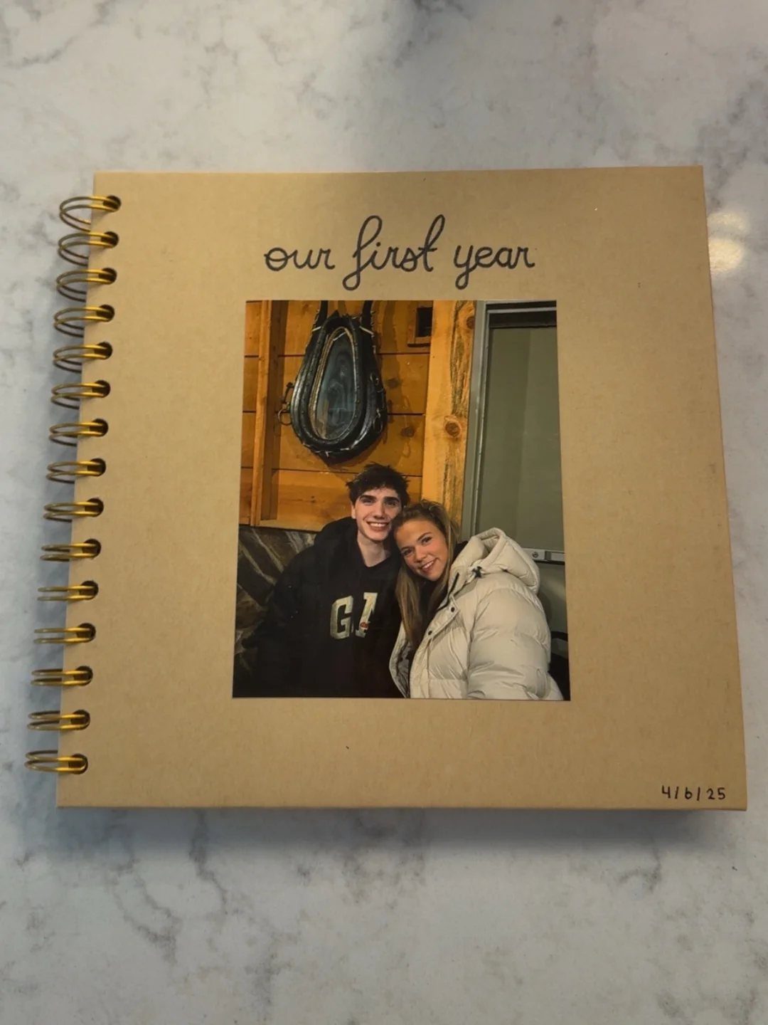 17 Anniversary Boyfriend Gifts He'll Actually Use (2026) 2 Brown spiral photo album with a couple's picture and 'our first year' text.