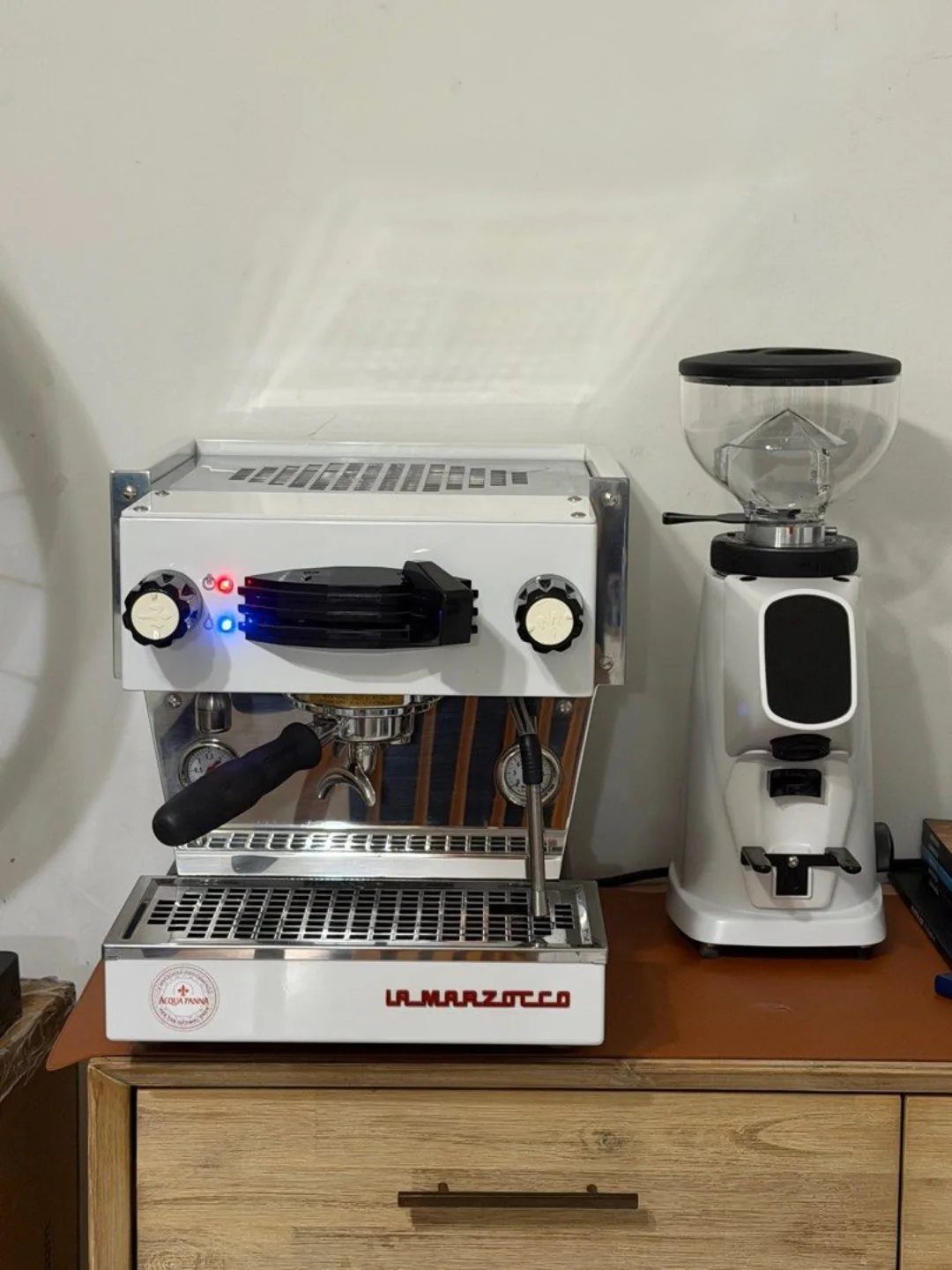 17 Anniversary Boyfriend Gifts He'll Actually Use (2026) 11 White La Marzocco espresso machine and coffee grinder on a wooden cabinet.