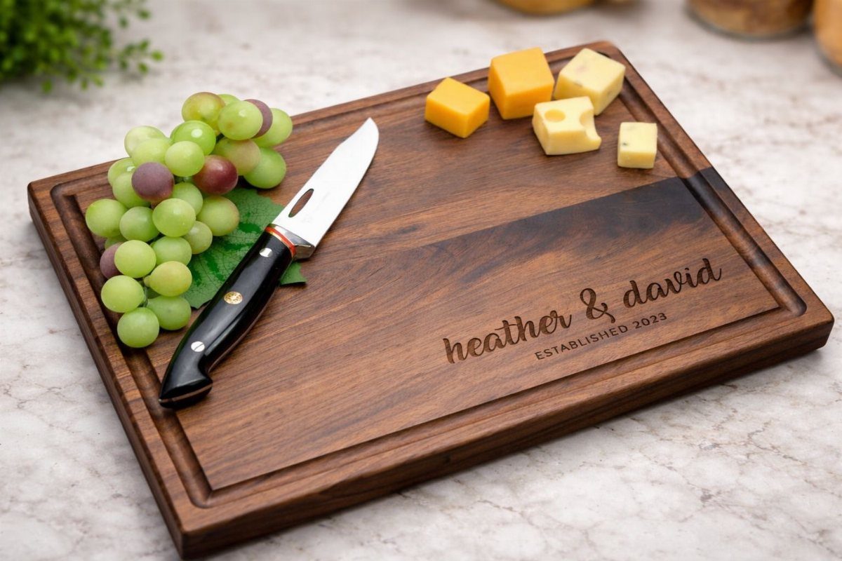 17 Anniversary Boyfriend Gifts He'll Actually Use (2026) 6 Personalized wooden cutting board with engraved names, grapes, cheese, and a knife.