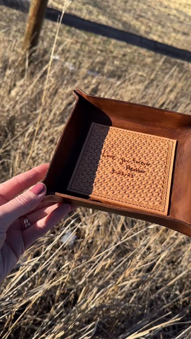 17 Anniversary Boyfriend Gifts He'll Actually Use (2026) 8 Brown leather valet tray with a personalized engraved message held over dry grass.