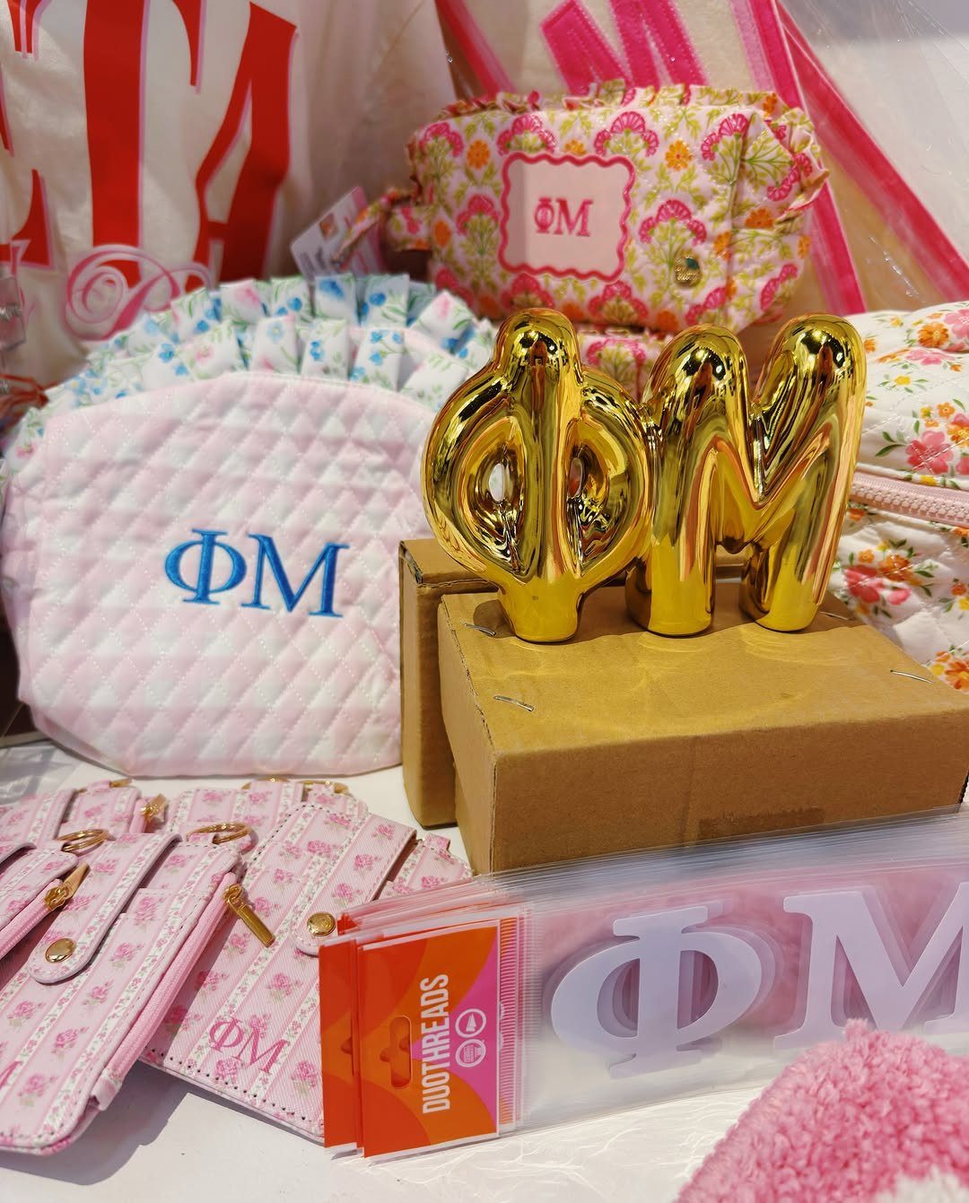 Quilted white bag and gold Greek letters Phi Mu among pink sorority accessories.