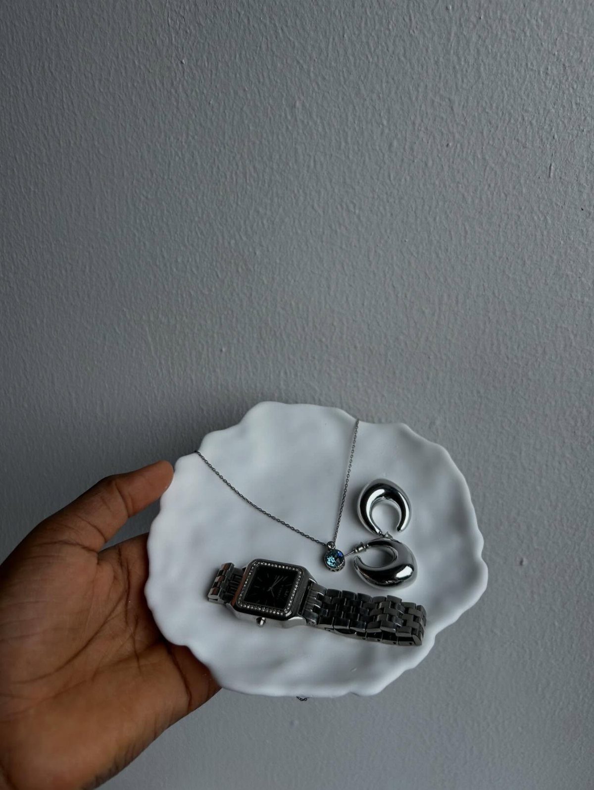 White ceramic jewelry dish holding a silver watch, necklace, and hoop earrings.