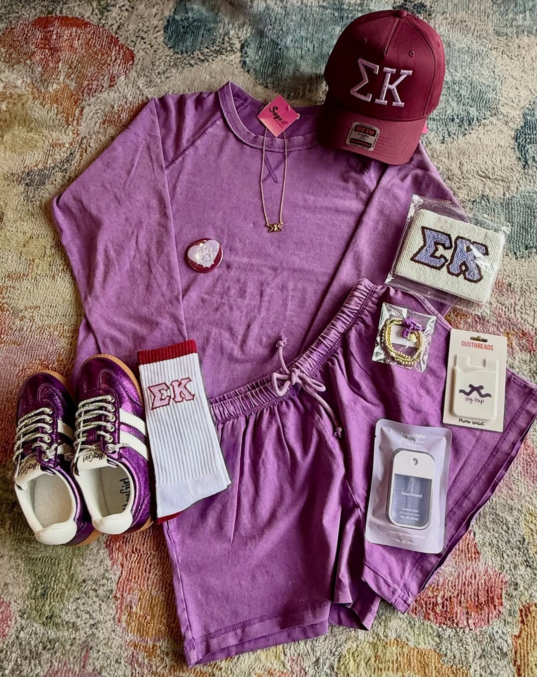 Purple clothing set with matching accessories and sneakers on a colorful patterned rug.