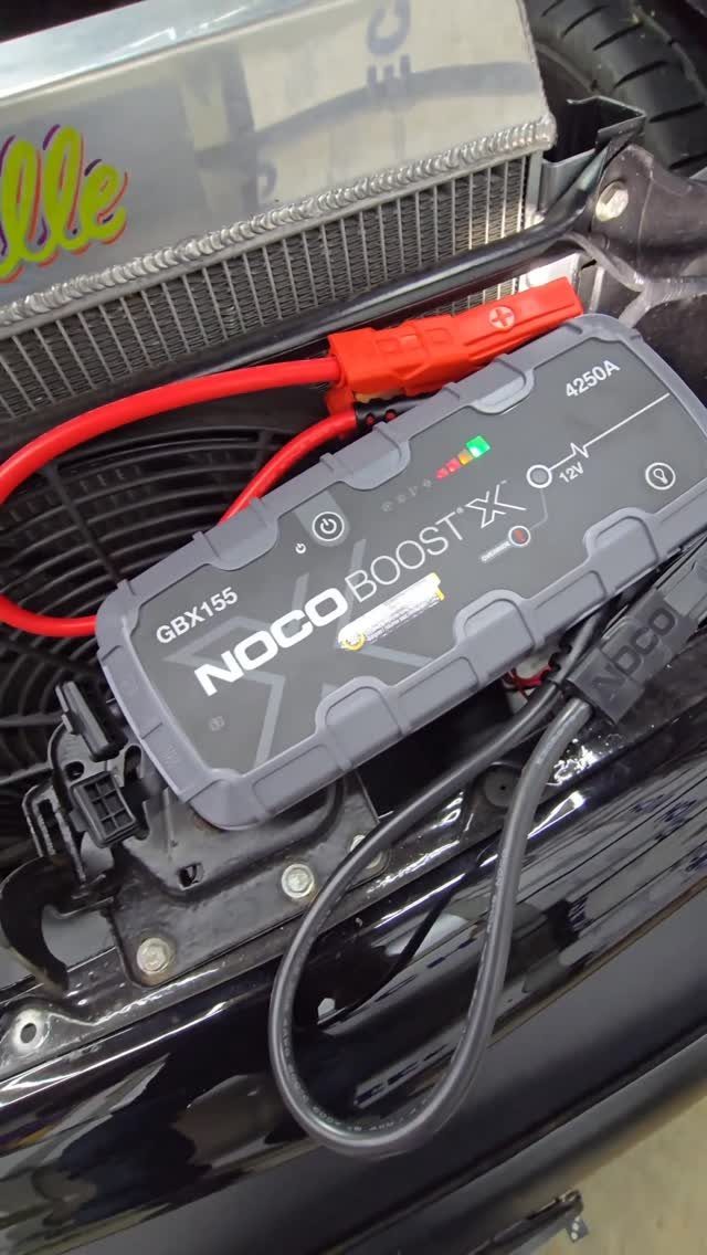 13 Ideas for a Birthday Gift for a Man Who Has Everything 2 NOCO Boost portable jump starter connected to a vehicle engine bay with cables.