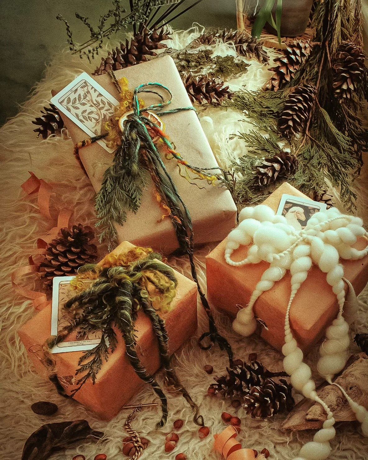 Birthday Gift Wrapping Ideas: 9 Ways to Wrap a Present 4 Wrapped gifts decorated with yarn and greenery resting on white fur with pinecones.