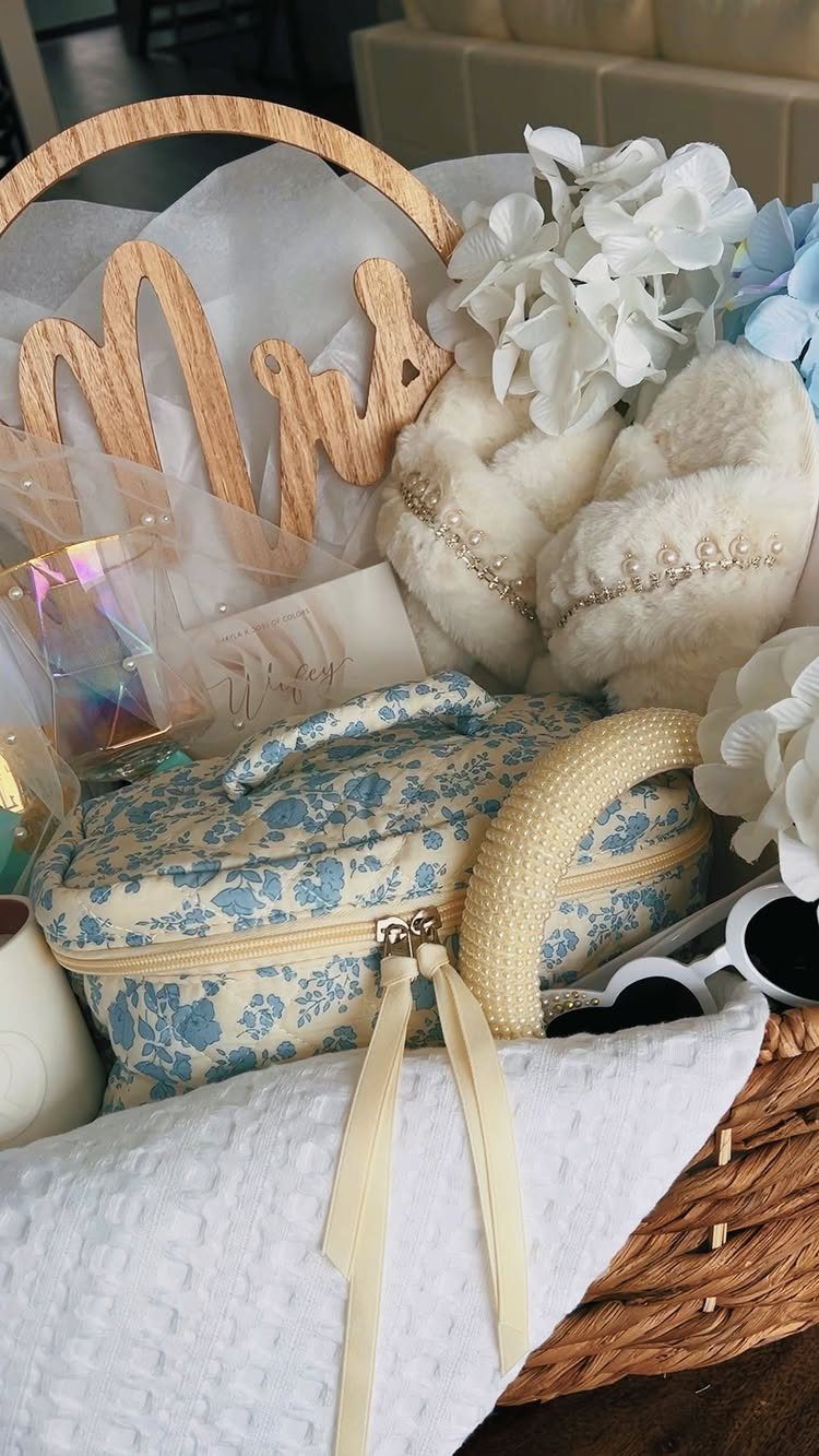 11 Bridal Shower Gift Basket Ideas for Every Bride-to-Be 3 Wicker gift basket containing a blue floral bag, white slippers, and Mrs sign.