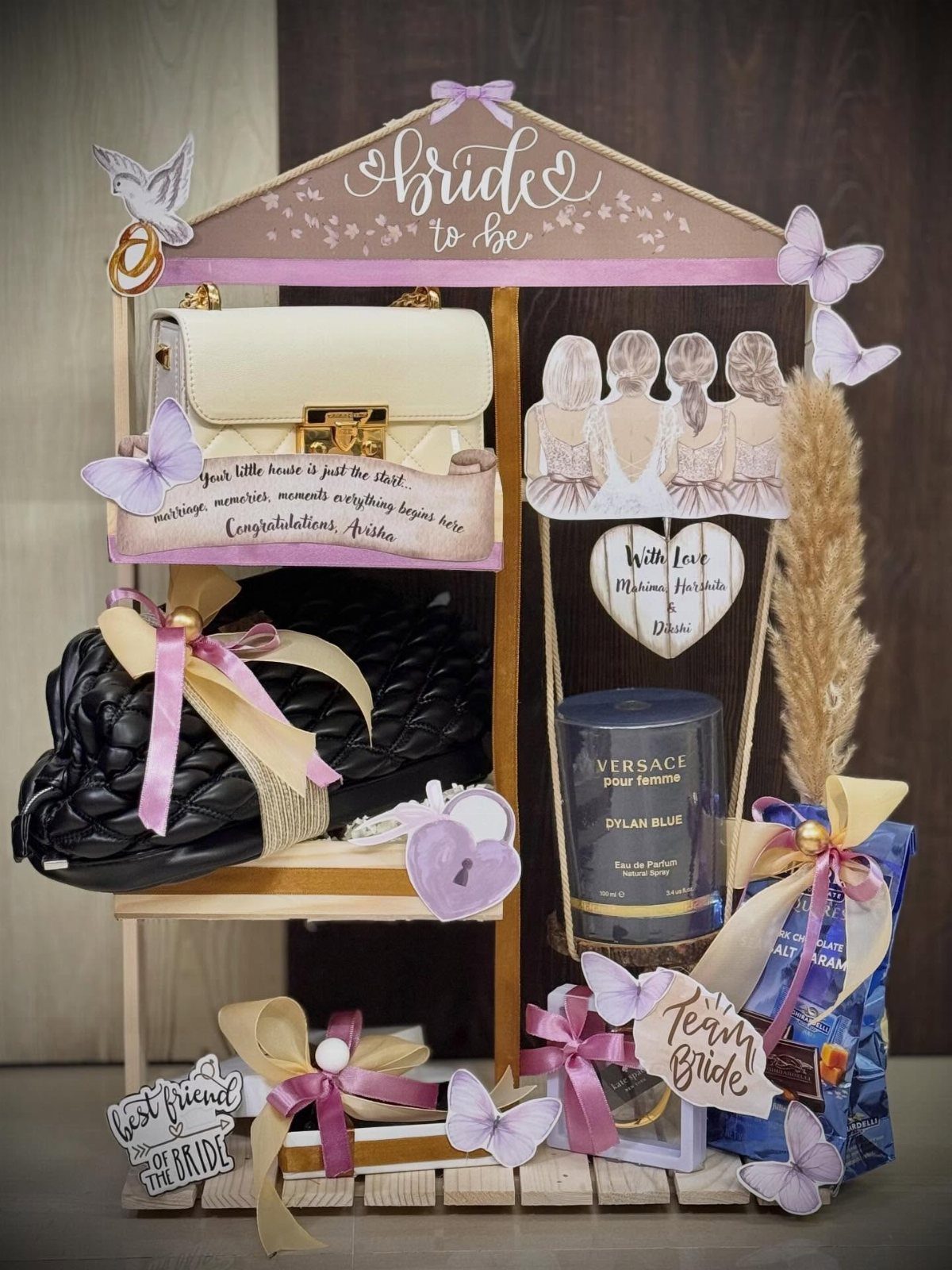 11 Bridal Shower Gift Basket Ideas for Every Bride-to-Be 11 Wooden bridal gift display with handbags, perfume, and purple butterfly decorations.