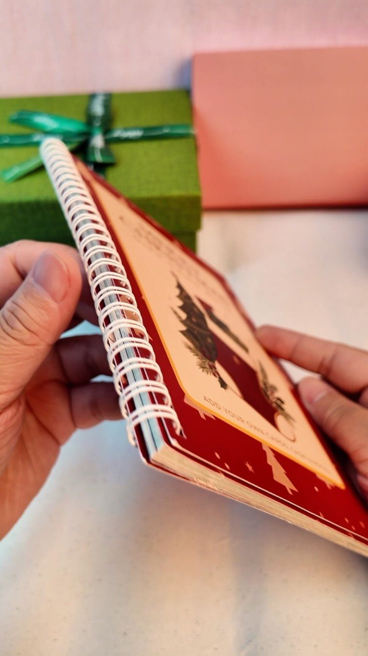 Red spiral notebook with Christmas cover held by hands near a green gift.