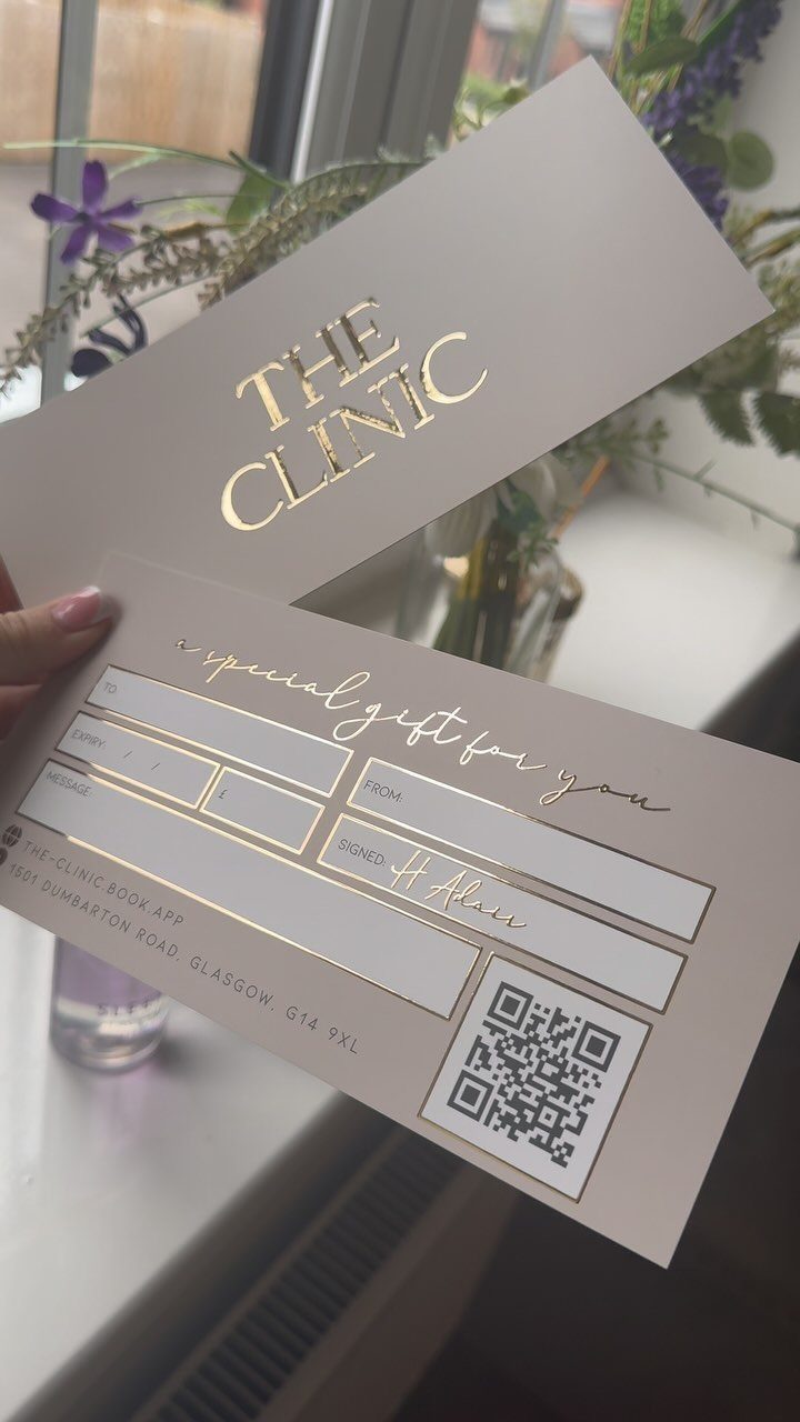 White gift certificate with gold foil lettering held by a hand near flowers.