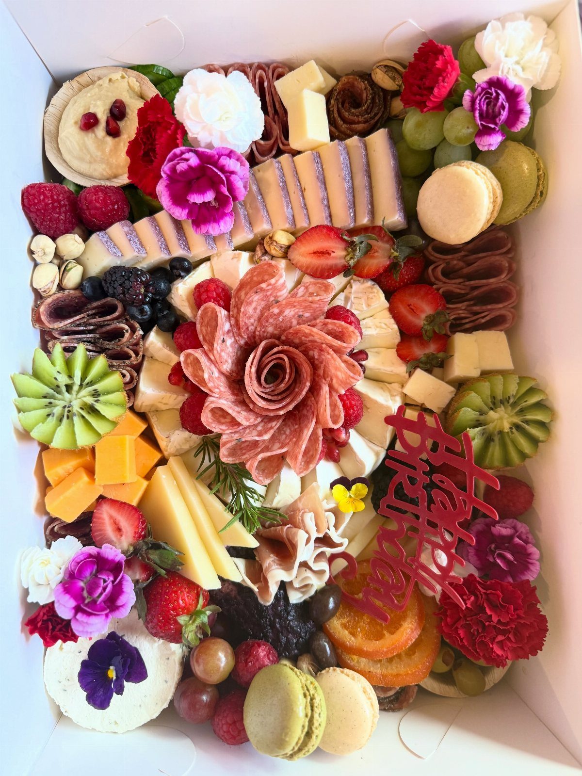 Charcuterie gift box with meats, cheeses, fruits, and a red Happy Birthday topper.