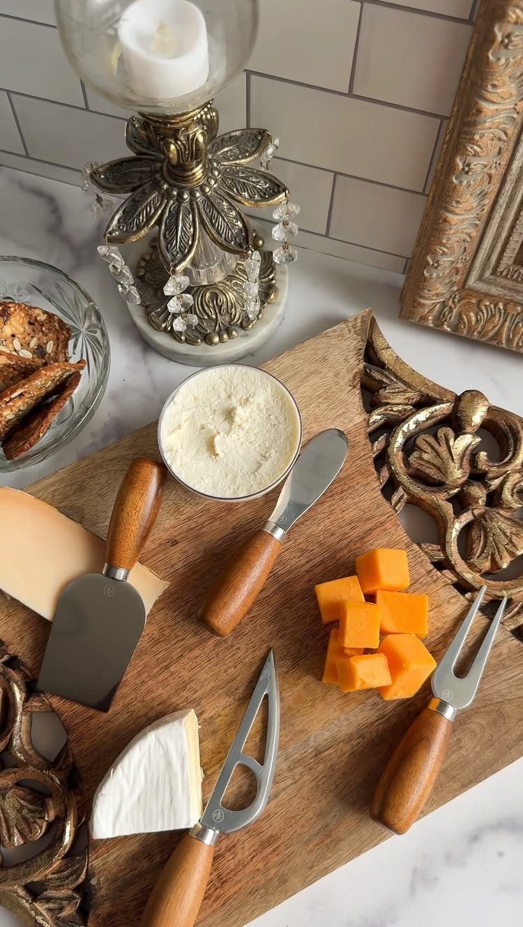 Three wooden-handled cheese knives on a board with brie and cheddar cubes.