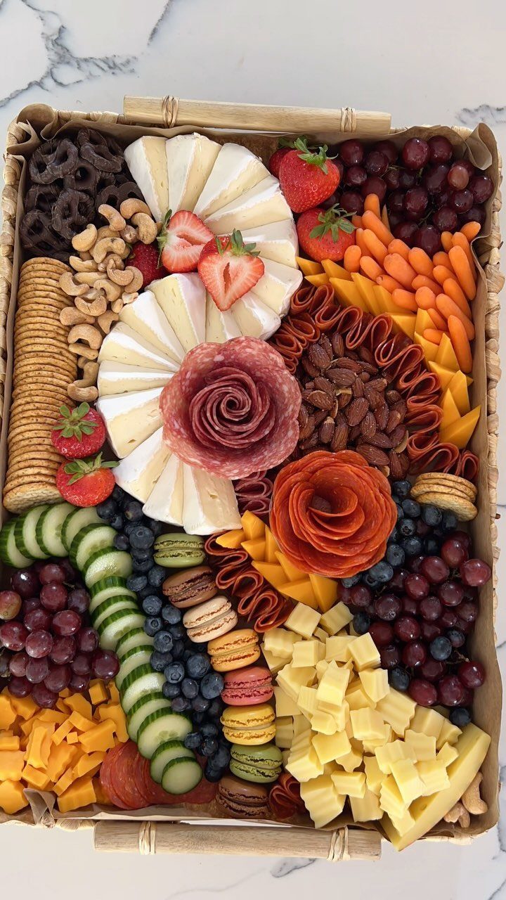 Charcuterie basket with meats, cheeses, fresh fruits, vegetables, and colorful macarons on marble.