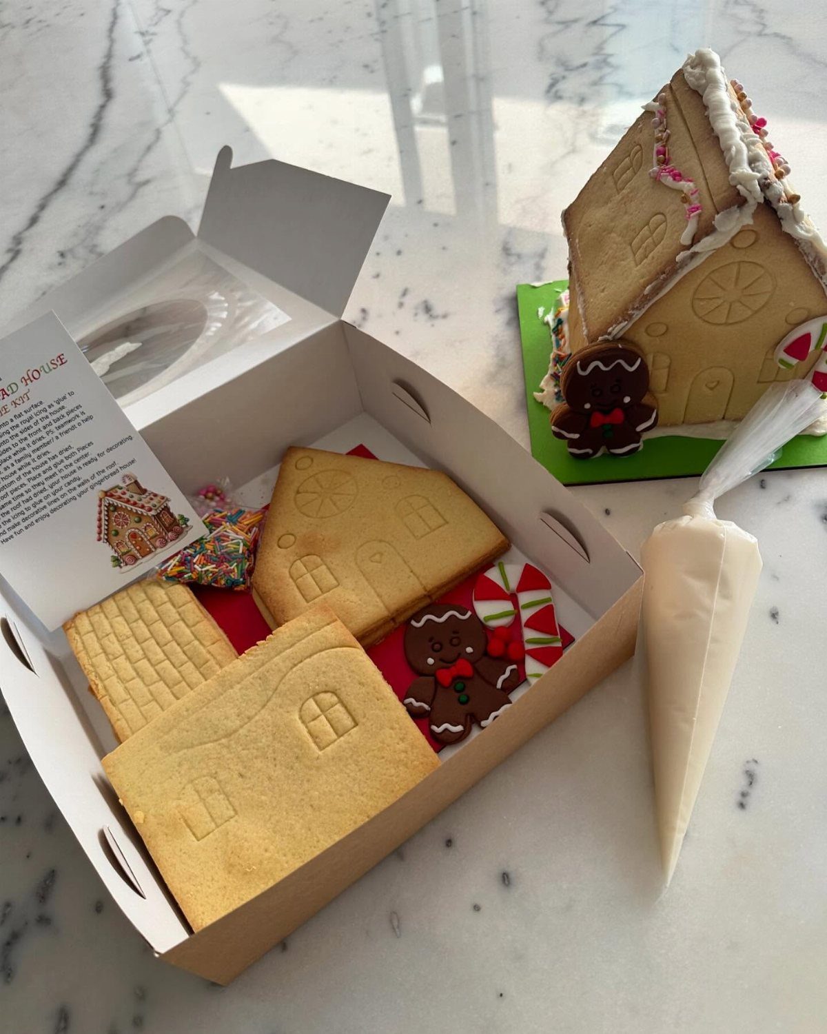 Christmas Food Basket Gift Ideas: 10 Options to Give 10 Gingerbread house kit in a box next to a finished decorated gingerbread house.