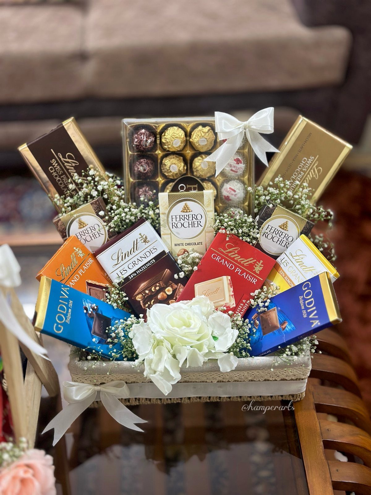 Christmas Gift Baskets for Family: 7 Ideas for Every Age 2 Woven gift basket filled with assorted chocolate bars and truffles decorated with white flowers.