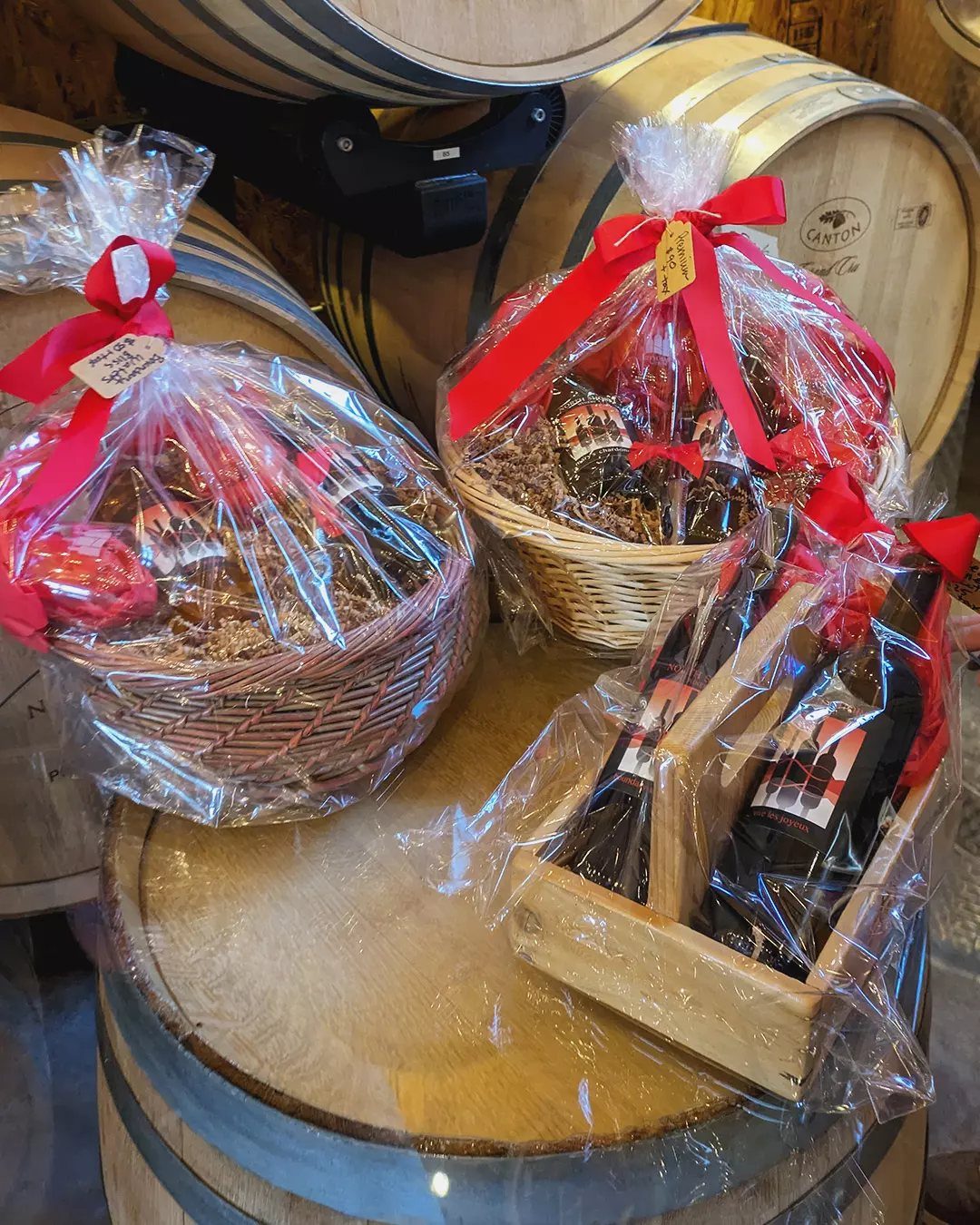 Christmas Gift Baskets for Family: 7 Ideas for Every Age 5 Gift baskets with wine and gourmet treats wrapped in cellophane on wooden barrels