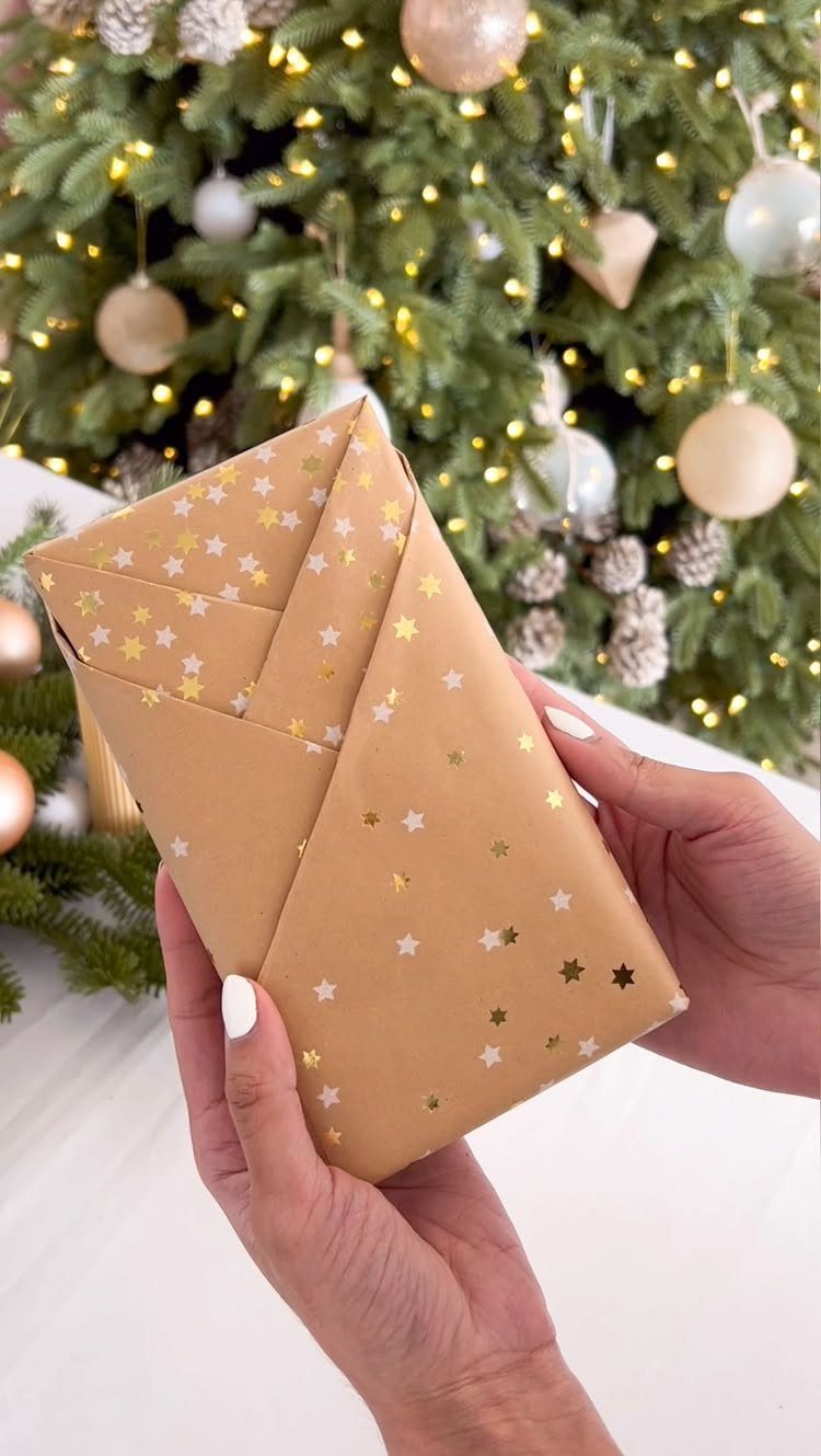 Christmas Gift Wrapping: 5 Ideas for Paper, Bows and Bags 1 Hands holding a brown star-patterned wrapped gift in front of a Christmas tree