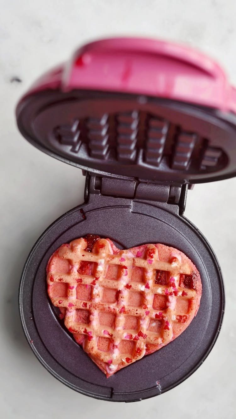 11 Christmas Gifts for Adults, From Waffle Makers to Desks 6 Heart-shaped pink waffle inside an open pink mini waffle maker on light surface