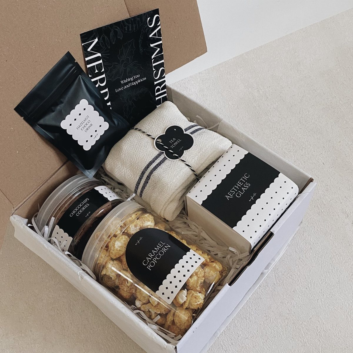 11 Christmas Gifts for Adults, From Waffle Makers to Desks 7 Christmas gift box containing caramel popcorn, cookies, a wrapped towel, and a card.