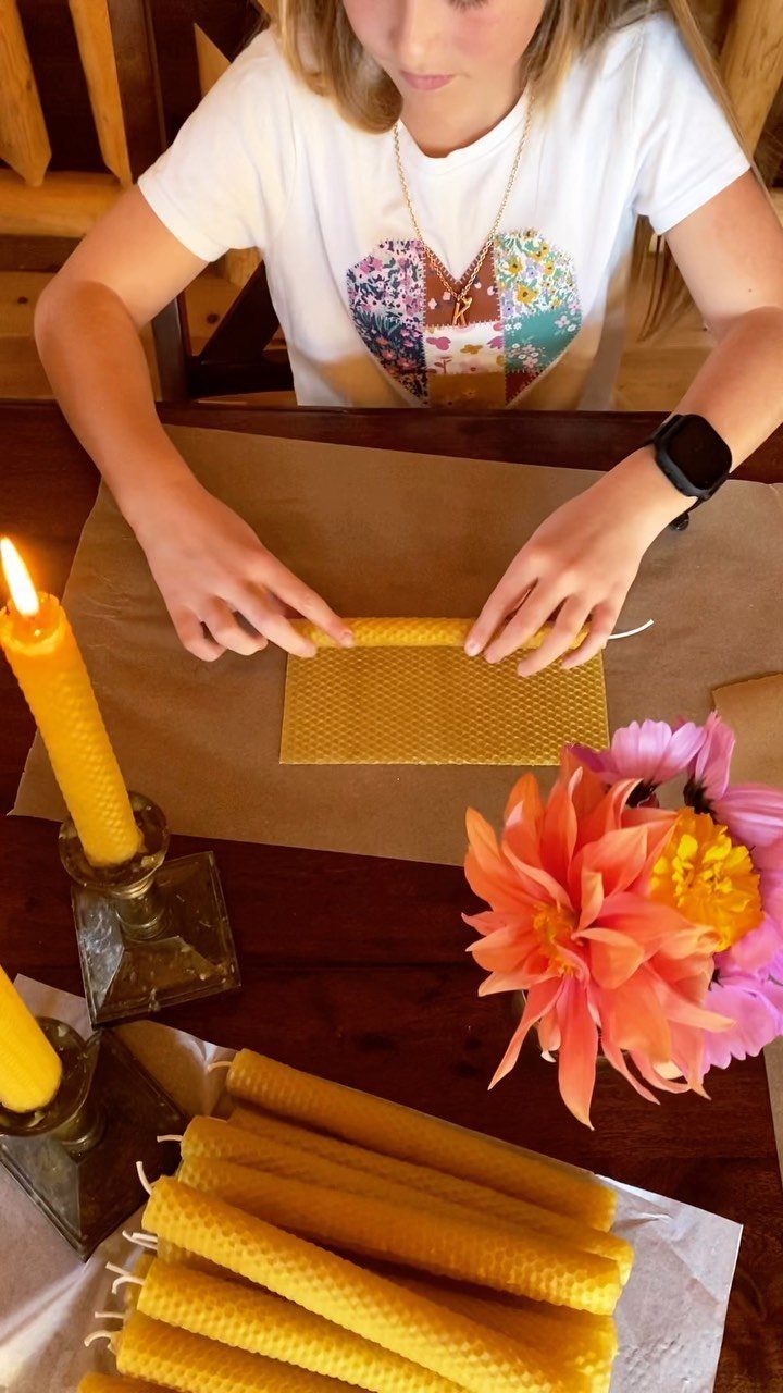 25 Christmas Gifts to Make at Home: Candles to Cookies 1 Woman rolling yellow beeswax sheets into candles on a wooden table with flowers.
