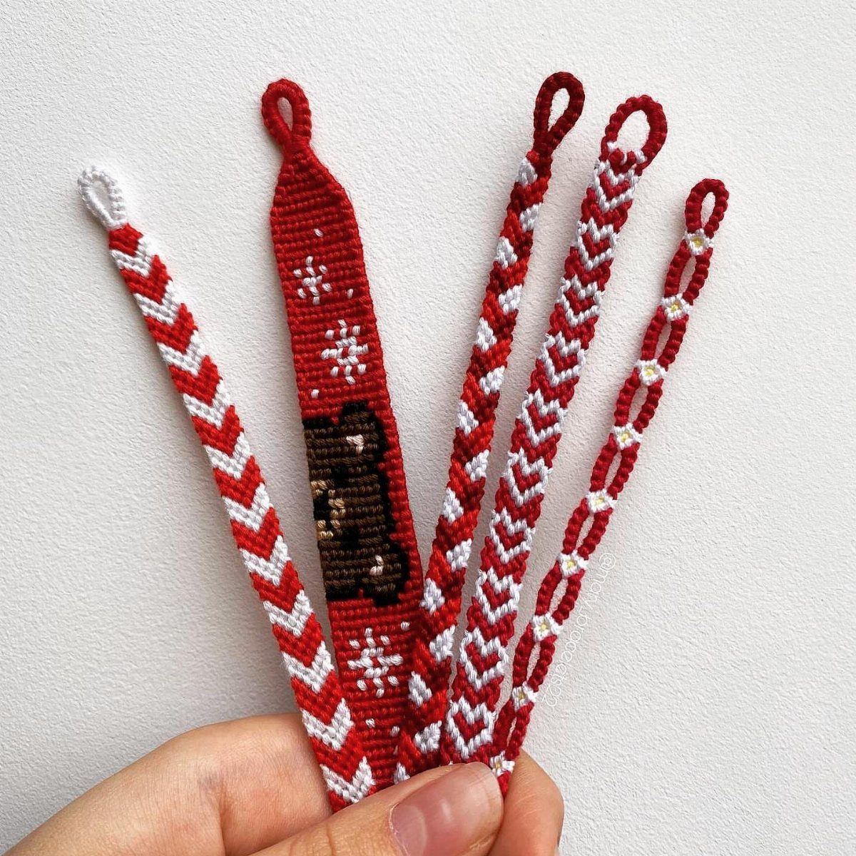 25 Christmas Gifts to Make at Home: Candles to Cookies 15 Hand holding five red and white woven friendship bracelets, one with a bear design.