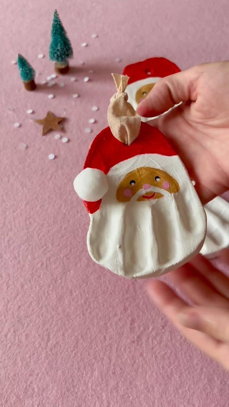 25 Christmas Gifts to Make at Home: Candles to Cookies 19 Handmade clay Santa Claus ornament held against a pink background with miniature trees.