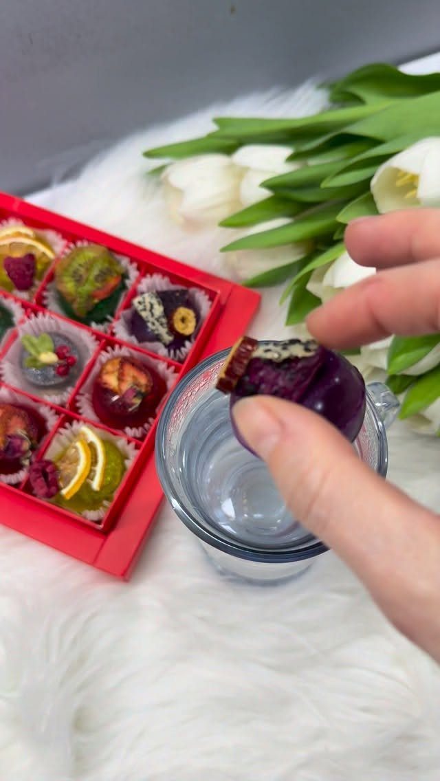 25 Christmas Gifts to Make at Home: Candles to Cookies 21 Hand holding a purple chocolate truffle next to a red box of assorted chocolates.