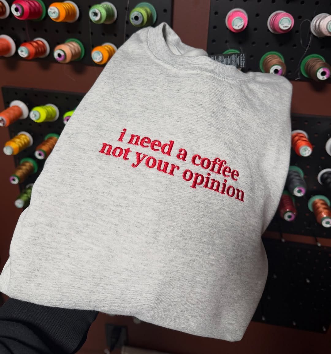 7 Coffee Gift Ideas for the Caffeine Fan on Your List 5 Grey sweatshirt with red embroidered coffee quote held against colorful thread spools.
