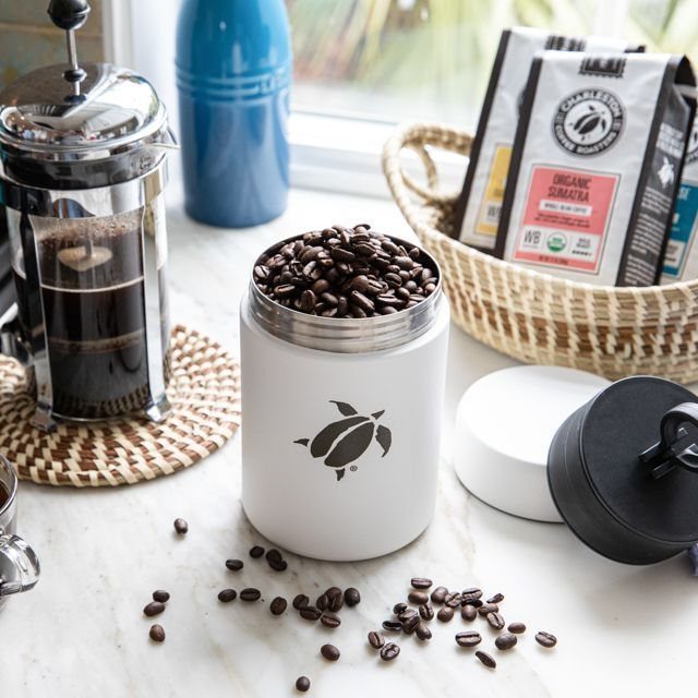 7 Coffee Gift Ideas for the Caffeine Fan on Your List 7 White coffee storage canister filled with beans on a marble countertop with accessories.