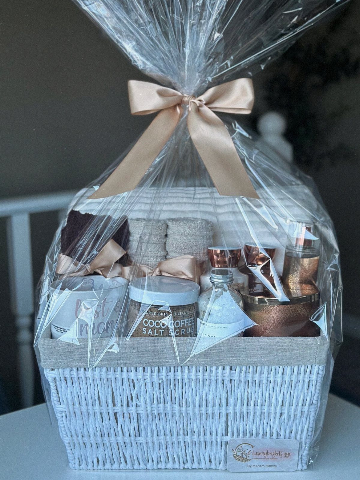 10 Cozy Gift Basket Ideas, from Spa Sets to Pumpkin Spice 2 White wicker spa gift basket with salt scrub and towels wrapped in cellophane.