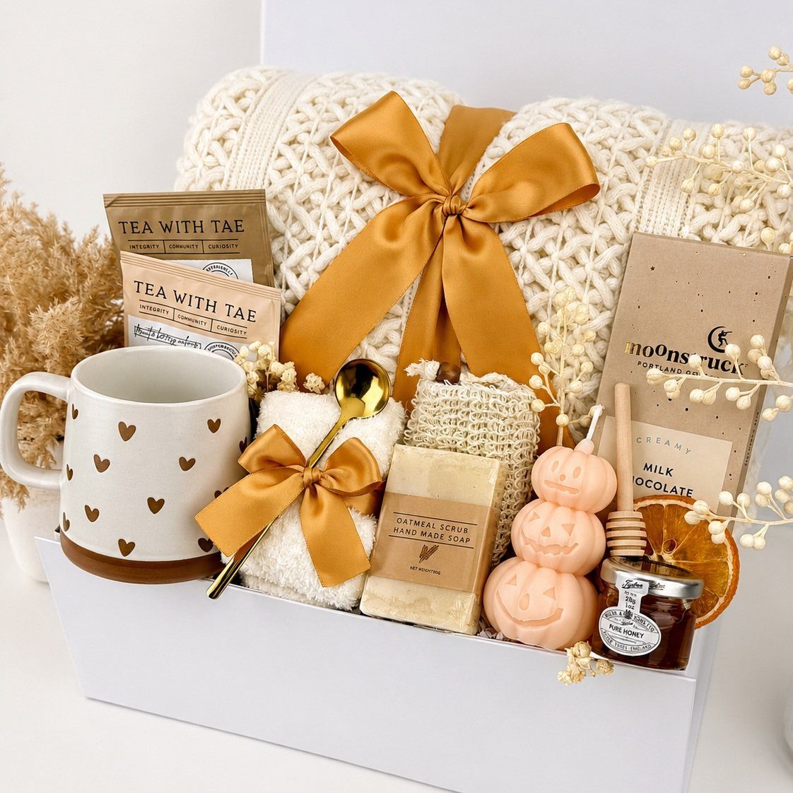 10 Cozy Gift Basket Ideas, from Spa Sets to Pumpkin Spice 4 White gift box with a knit blanket, heart-patterned mug, tea, and spa treats.