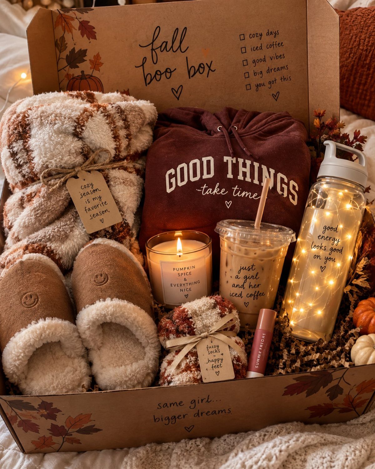 10 Cozy Gift Basket Ideas, from Spa Sets to Pumpkin Spice 1 Gift box containing a plaid blanket, maroon hoodie, fluffy slippers, and autumn-themed accessories.