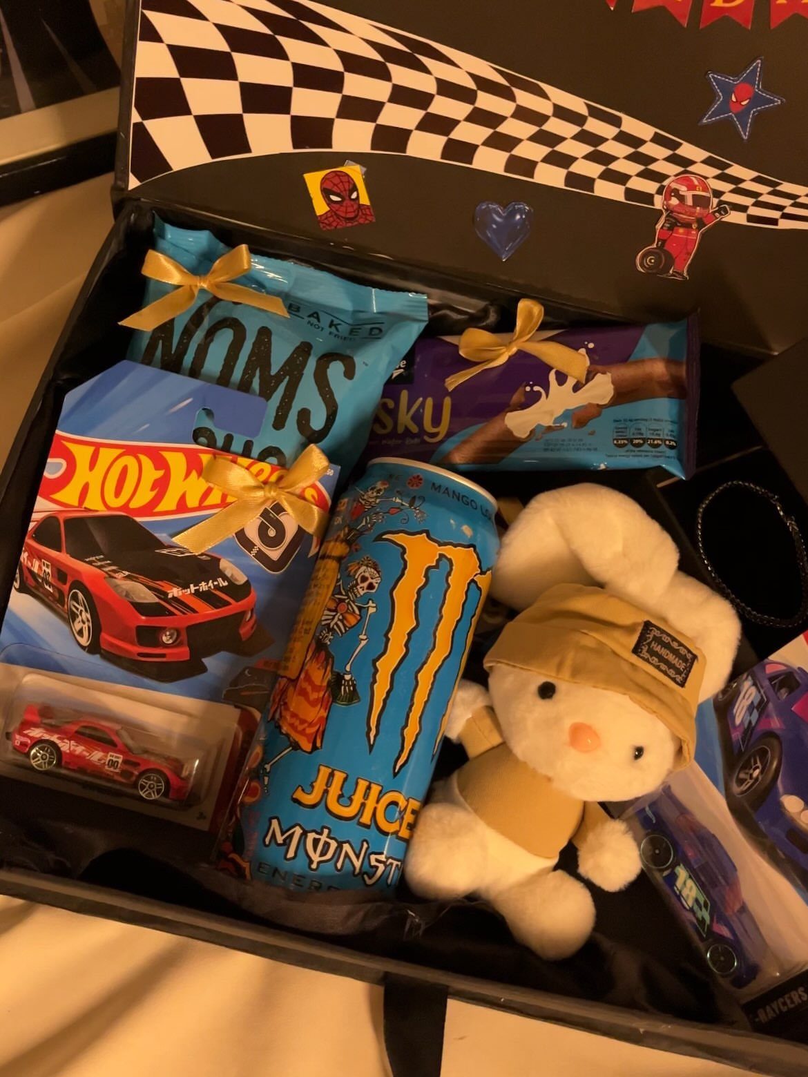17 Creative Birthday Gifts for Friends and Family 16 Gift box containing Hot Wheels cars, a plush bunny, and snacks with ribbons.