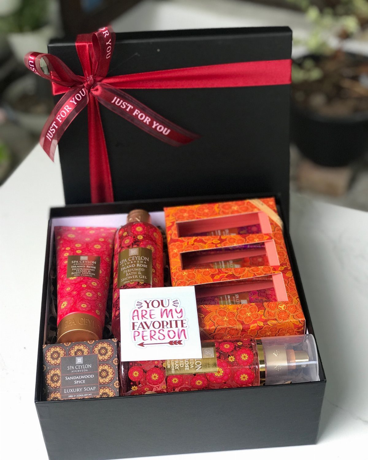 17 Creative Birthday Gifts for Friends and Family 4 Black gift box with red ribbon containing patterned bath and body pampering products.