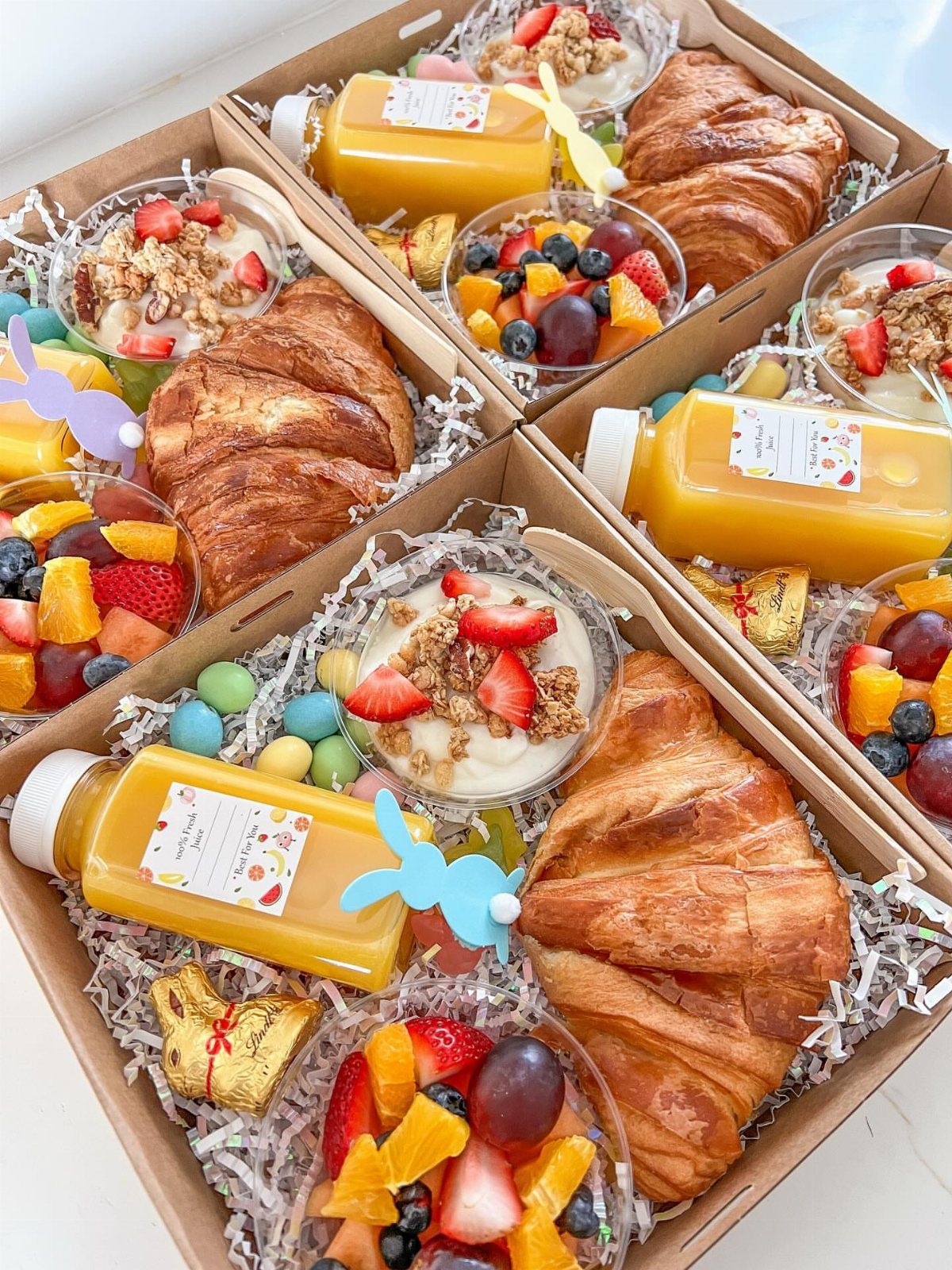 Easter Gift Box Ideas: 6 Options From Baskets to Bakery 2 Breakfast treat crates with croissants, fruit, juice, and Easter bunny decorations