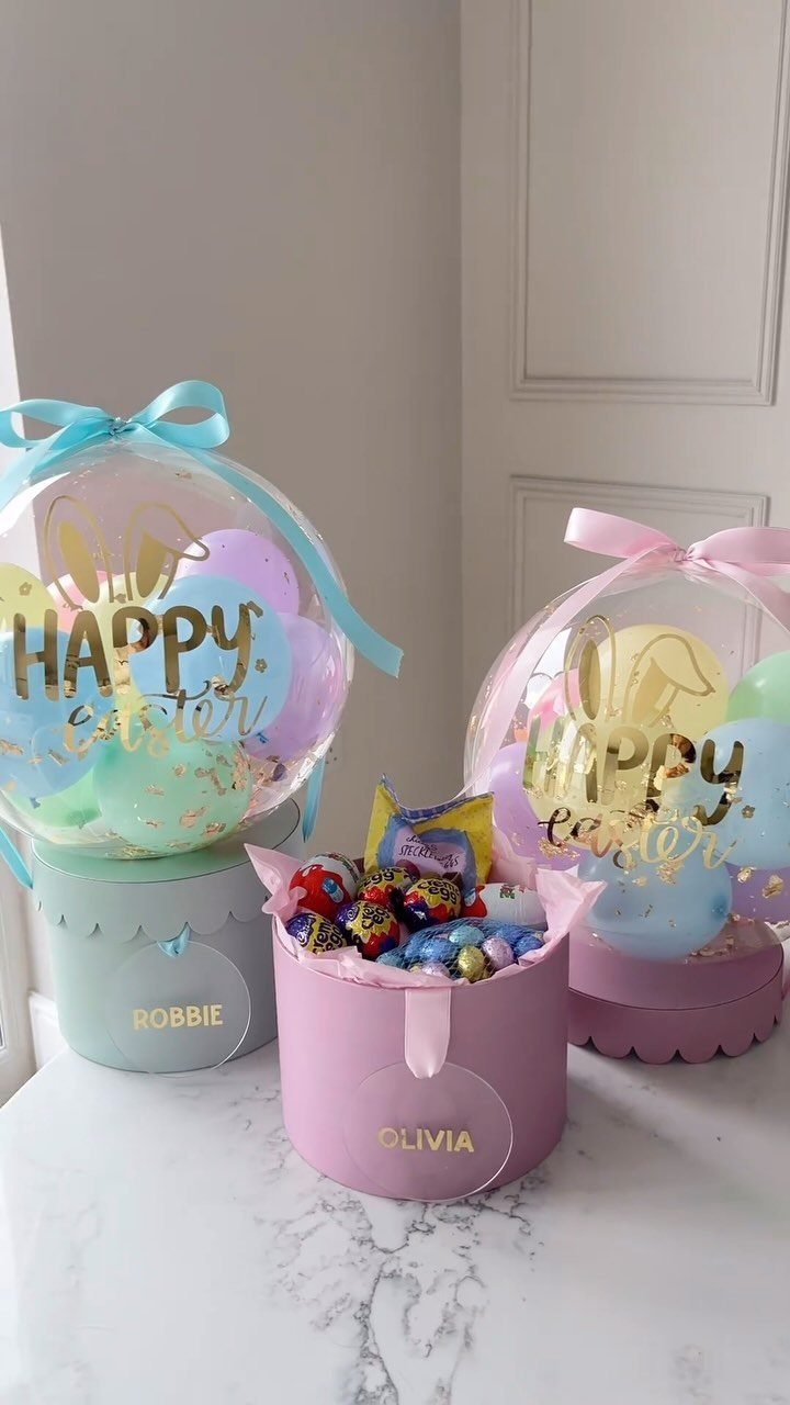 Easter Gift Box Ideas: 6 Options From Baskets to Bakery 3 Pastel Easter gift boxes with personalized name tags and Happy Easter balloons.