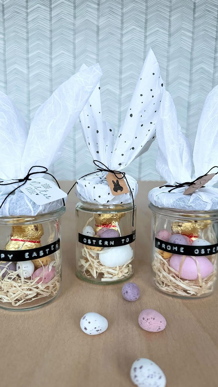 Three glass jars decorated as Easter bunnies with candy eggs and gold chocolates.