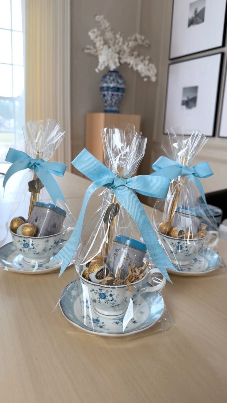 Floral teacups wrapped in cellophane with blue ribbons containing chocolates and small gifts.