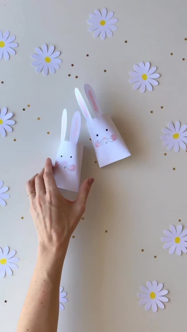 White paper bunny gift boxes on a surface with paper daisies and stars
