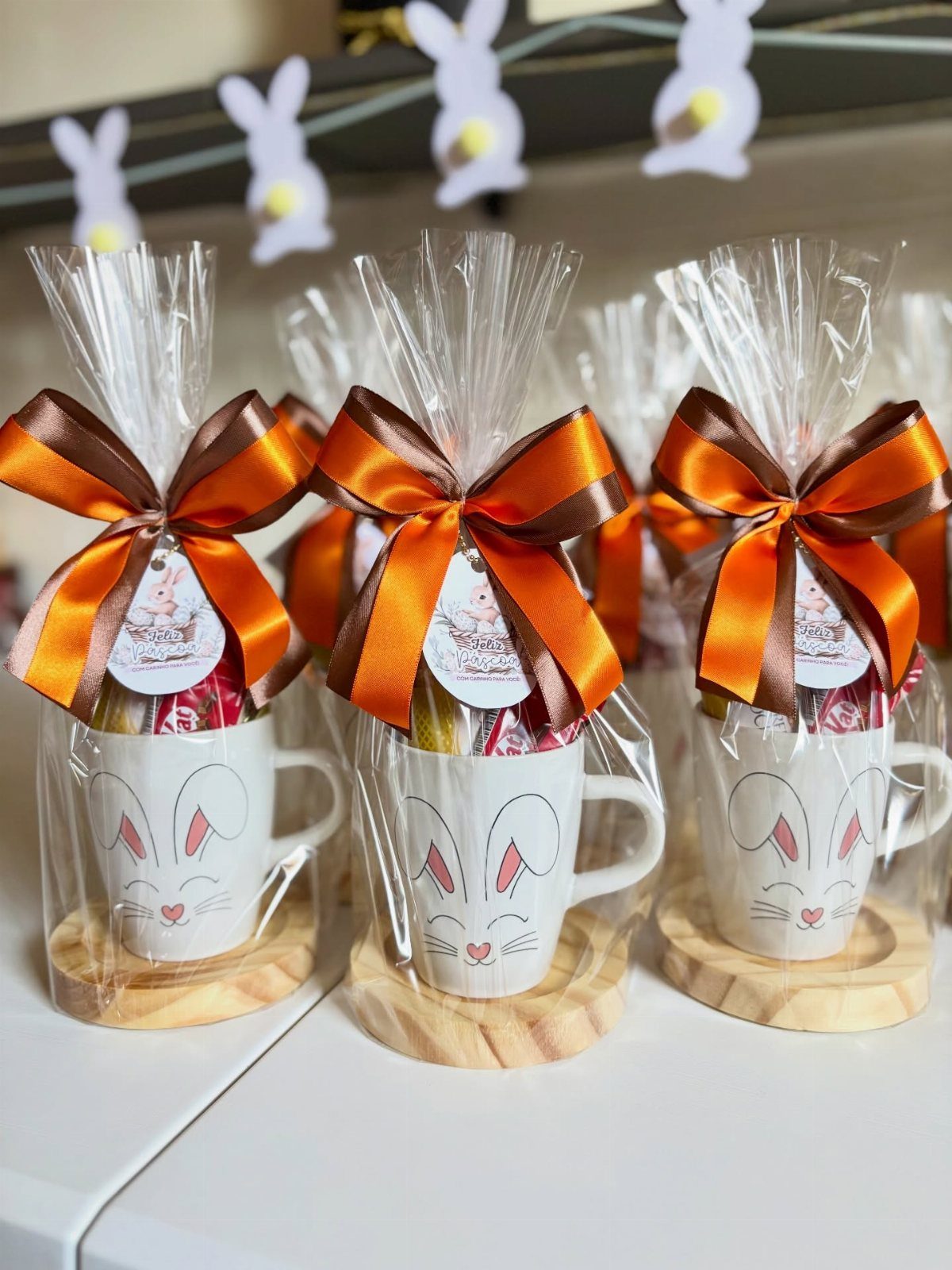 10 Easter Gifts for Young Adults They'll Actually Use 6 Easter gift sets with bunny mugs, treats, and orange ribbons on wooden coasters.