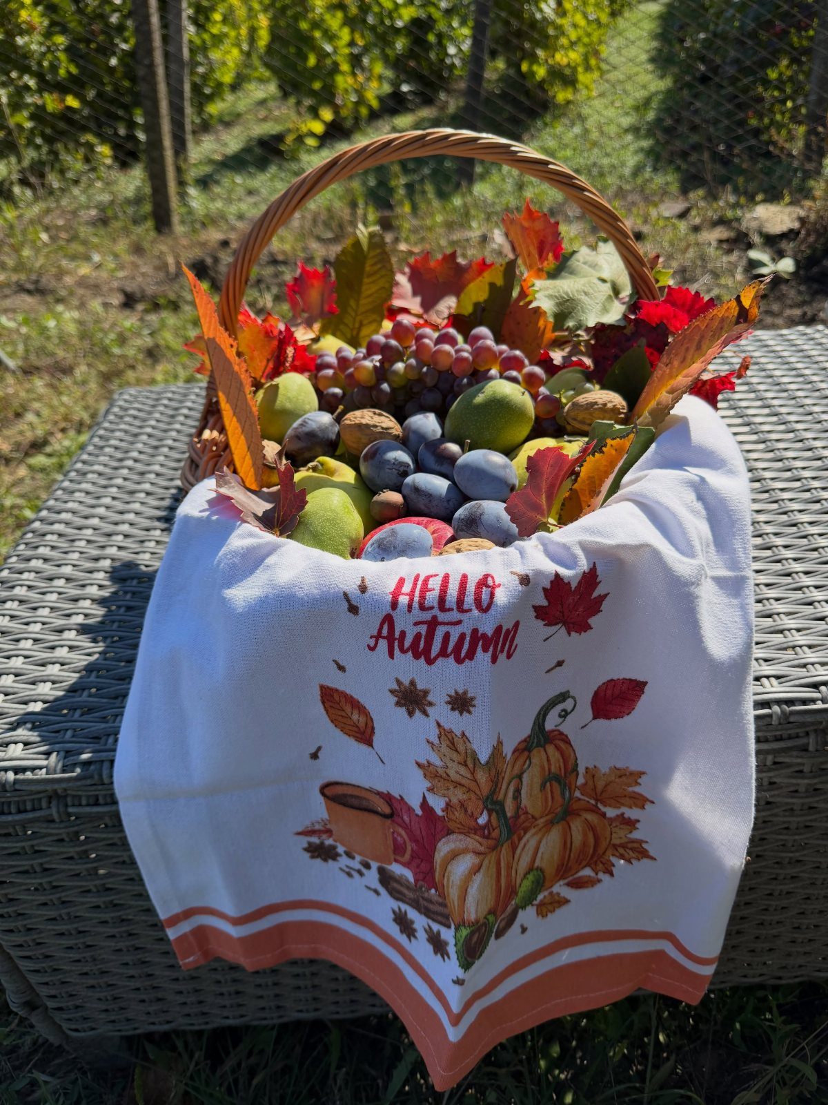 Wicker basket filled with autumn fruits and leaves draped with a pumpkin towel.