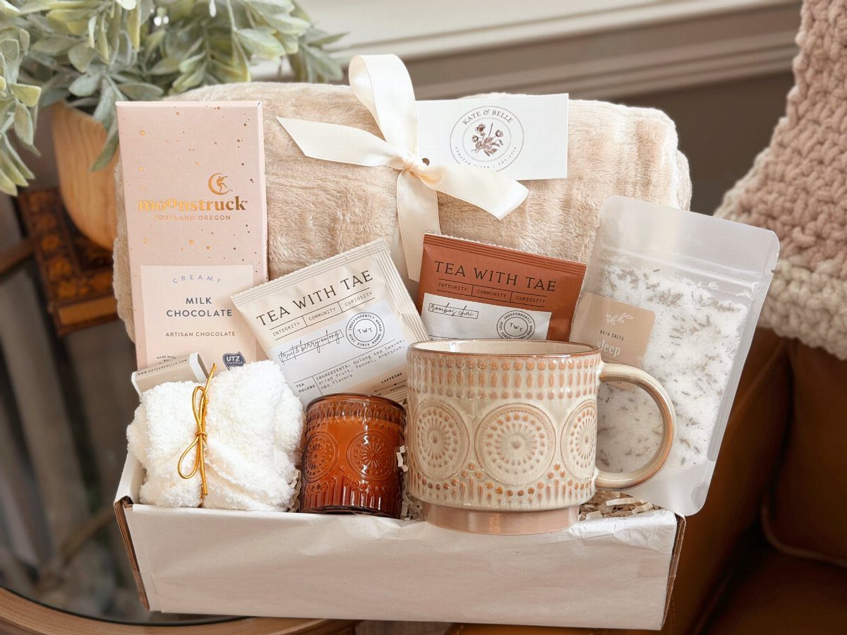 Cozy gift set with a beige blanket, patterned mug, tea, and candle in a box.