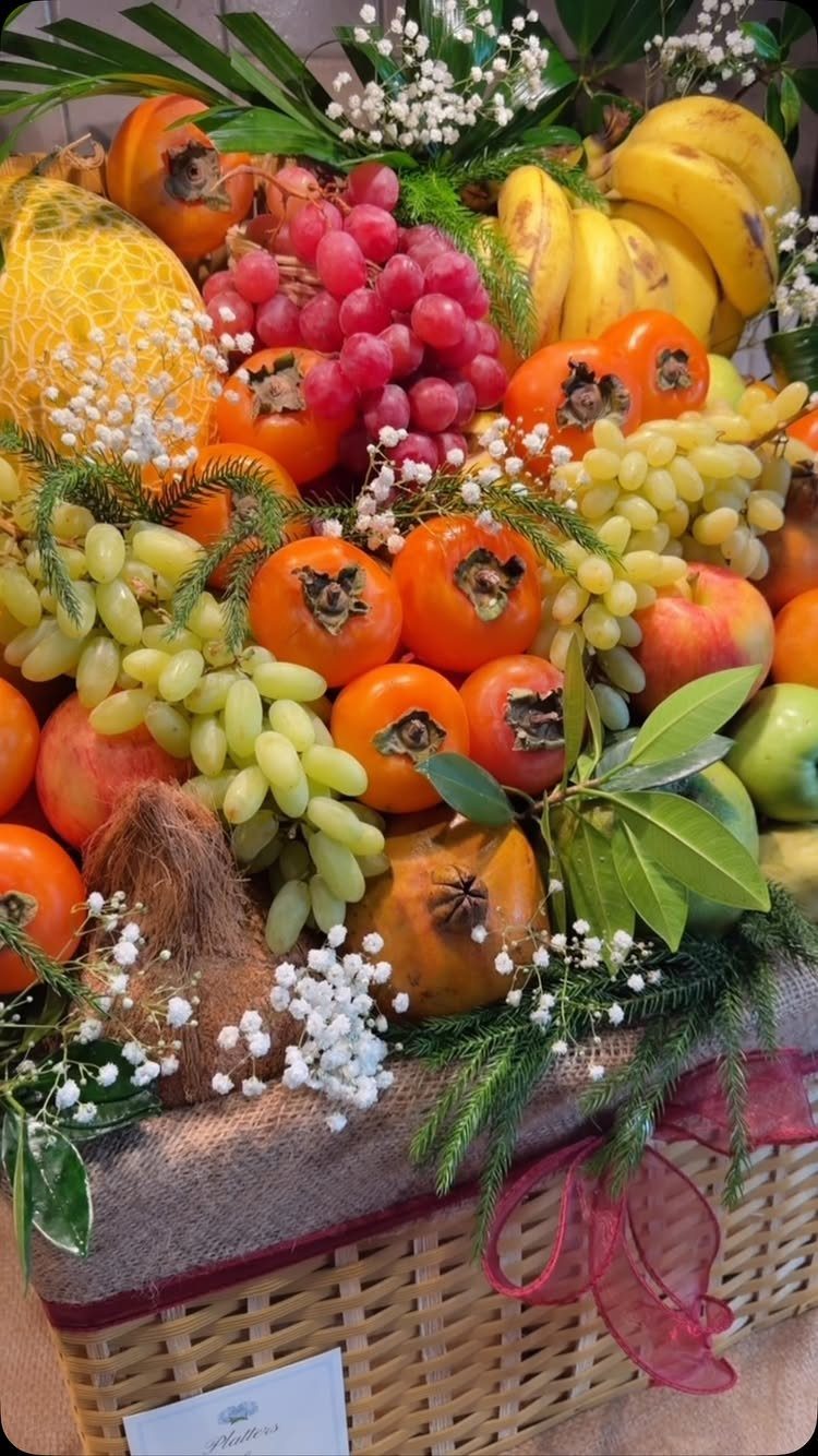 Woven wicker basket filled with grapes, persimmons, bananas, and apples with white flowers.