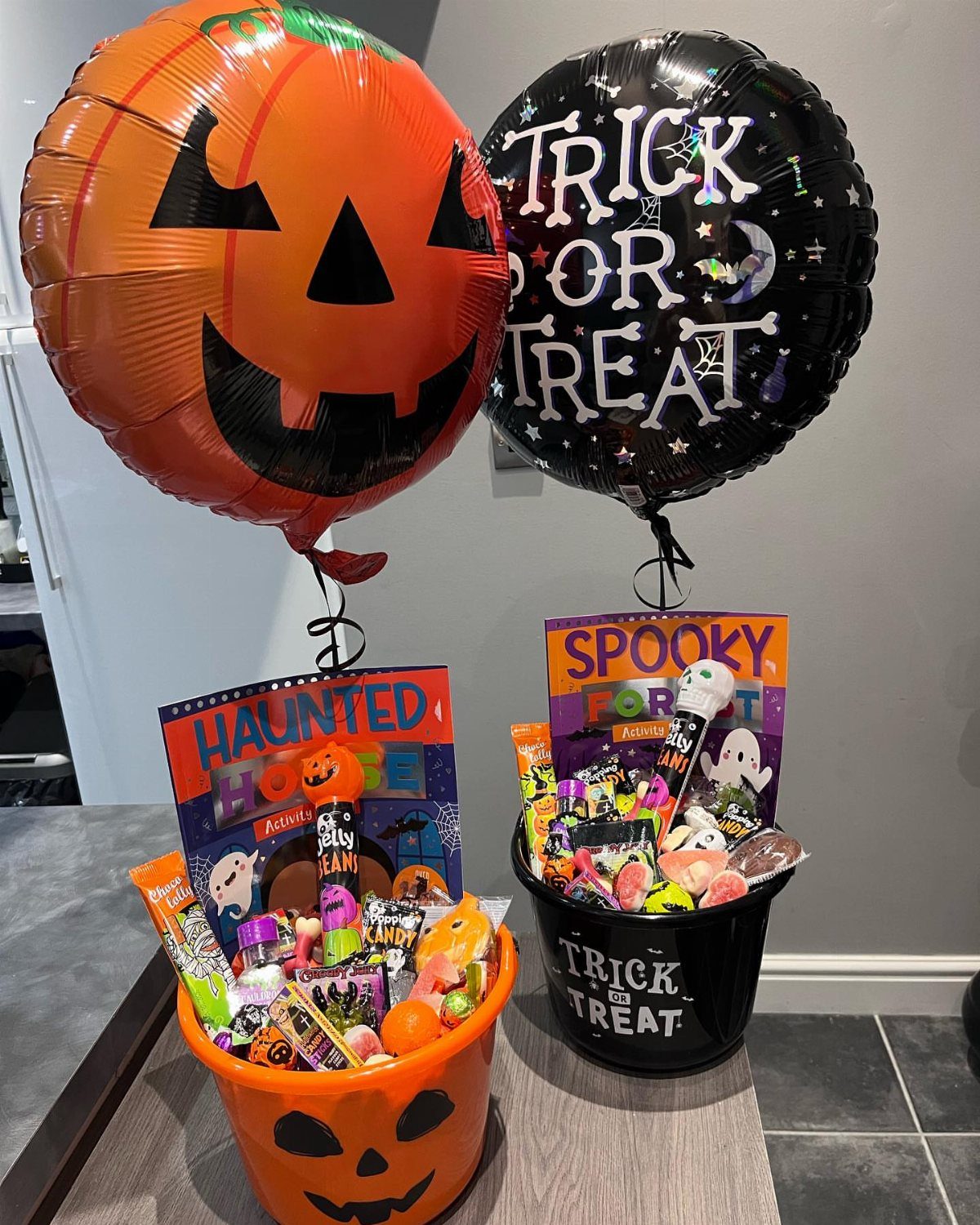 Two Halloween treat buckets filled with candy and topped with foil balloons.