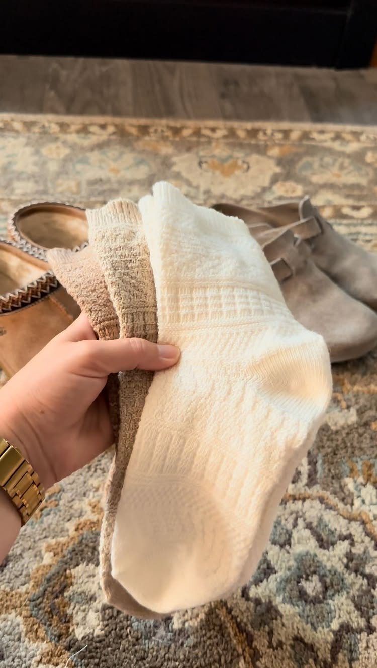 13 Fall Gifts for Women, From Cozy Socks to Cookbooks 4 Thick knitted cream and beige cozy socks held over a patterned rug.