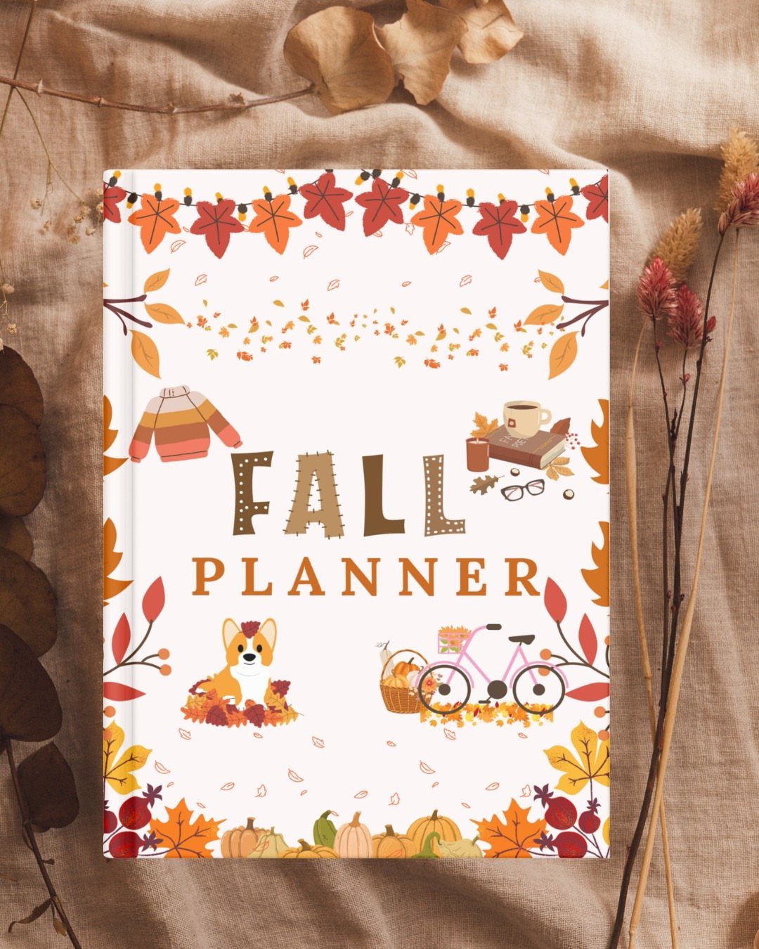 13 Fall Gifts for Women, From Cozy Socks to Cookbooks 11 Fall planner with autumn illustrations resting on beige linen with dried leaves